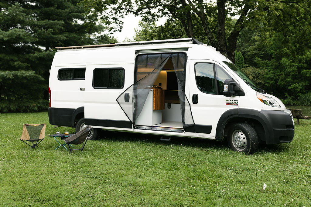 This white RV rental camper van is parked on lush grass, showcasing its open interior with a mesh screen and outdoor furniture. — photo 3