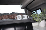 Inside a cozy RV rental, two camping mugs and a potted plant rest with a scenic view of red rock mountains.