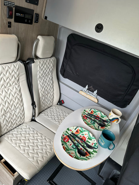 RV rental interior shows cream seats, a dining table set for two, a solar charge controller, and "The Mountains are calling me" decor.