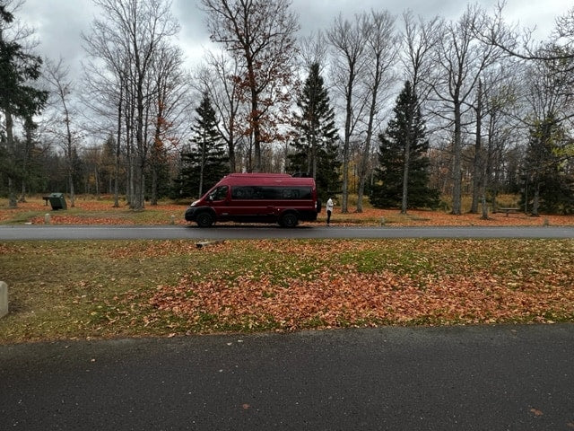  is pictured at night with a woman by its open side door.|Autumn RV rental: A red camper van is parked on a path in a park — photo 5