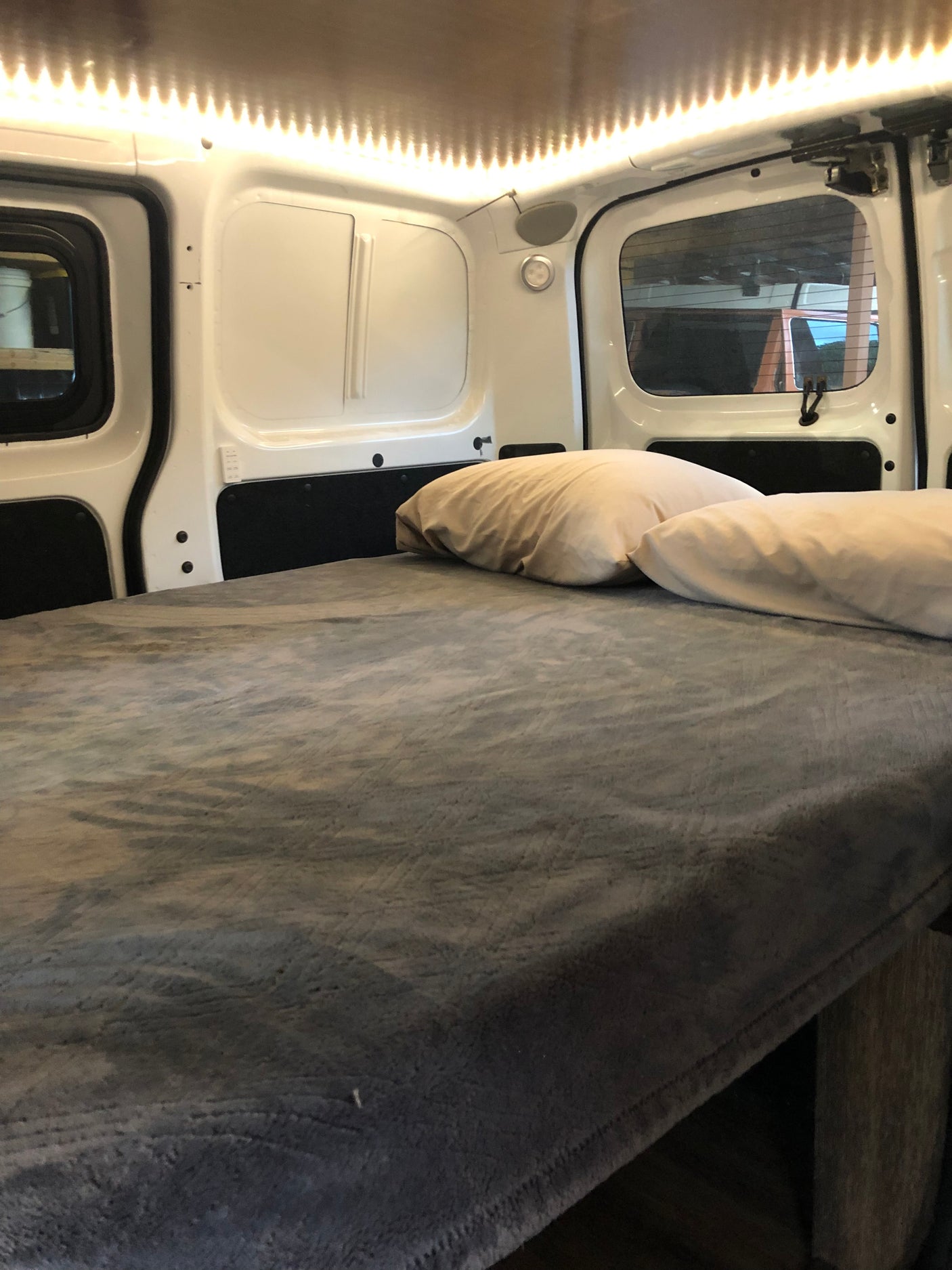 Interior of an RV rental camper van showing a comfortable bed with pillows under warm LED strip lighting.