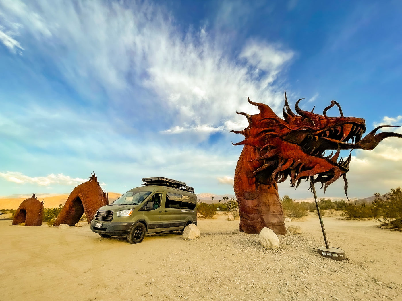 RV rental adventure: A green camper van rests near massive desert dragon sculptures under a bright sky. — photo 17