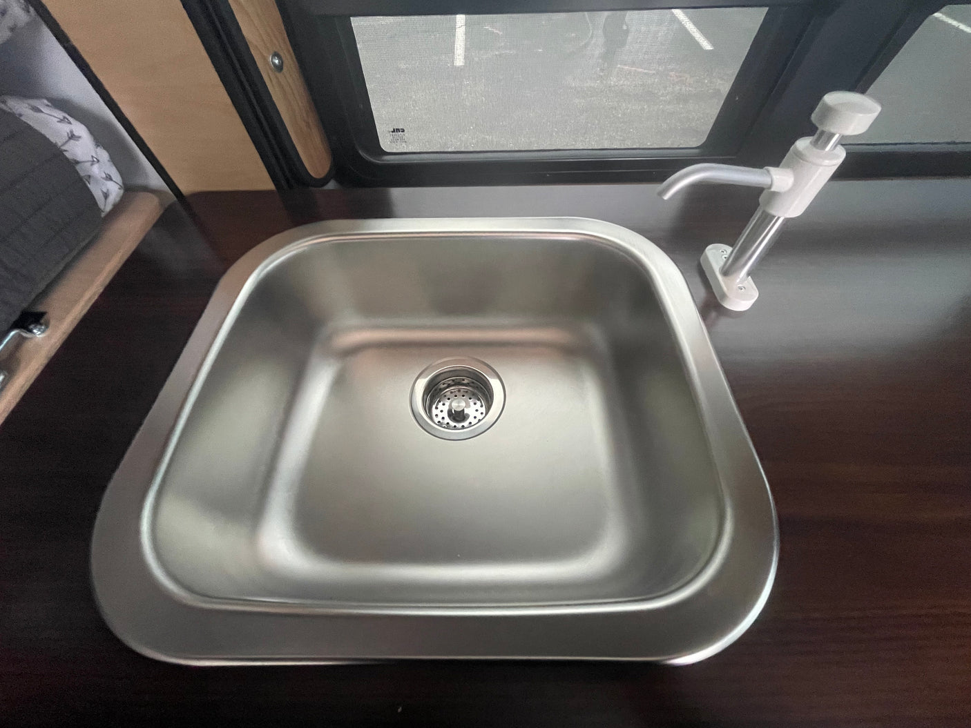 **RV rental** kitchen amenities: a stainless steel **sink** with pump **faucet** on a dark countertop. A window shows the outside.