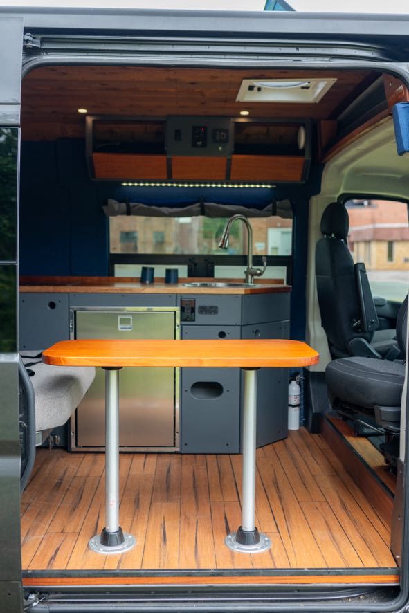 Inside a modern RV rental: a fully equipped kitchen with sink & fridge, wooden dining table, and cozy living space. — photo 4
