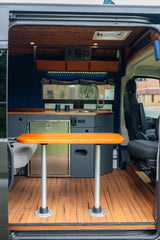 Inside a modern RV rental: a fully equipped kitchen with sink & fridge, wooden dining table, and cozy living space.