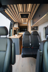 RV rental interior: A modern camper van with custom wood-slatted ceiling, LED lighting, sleek kitchen, and comfortable seating.
