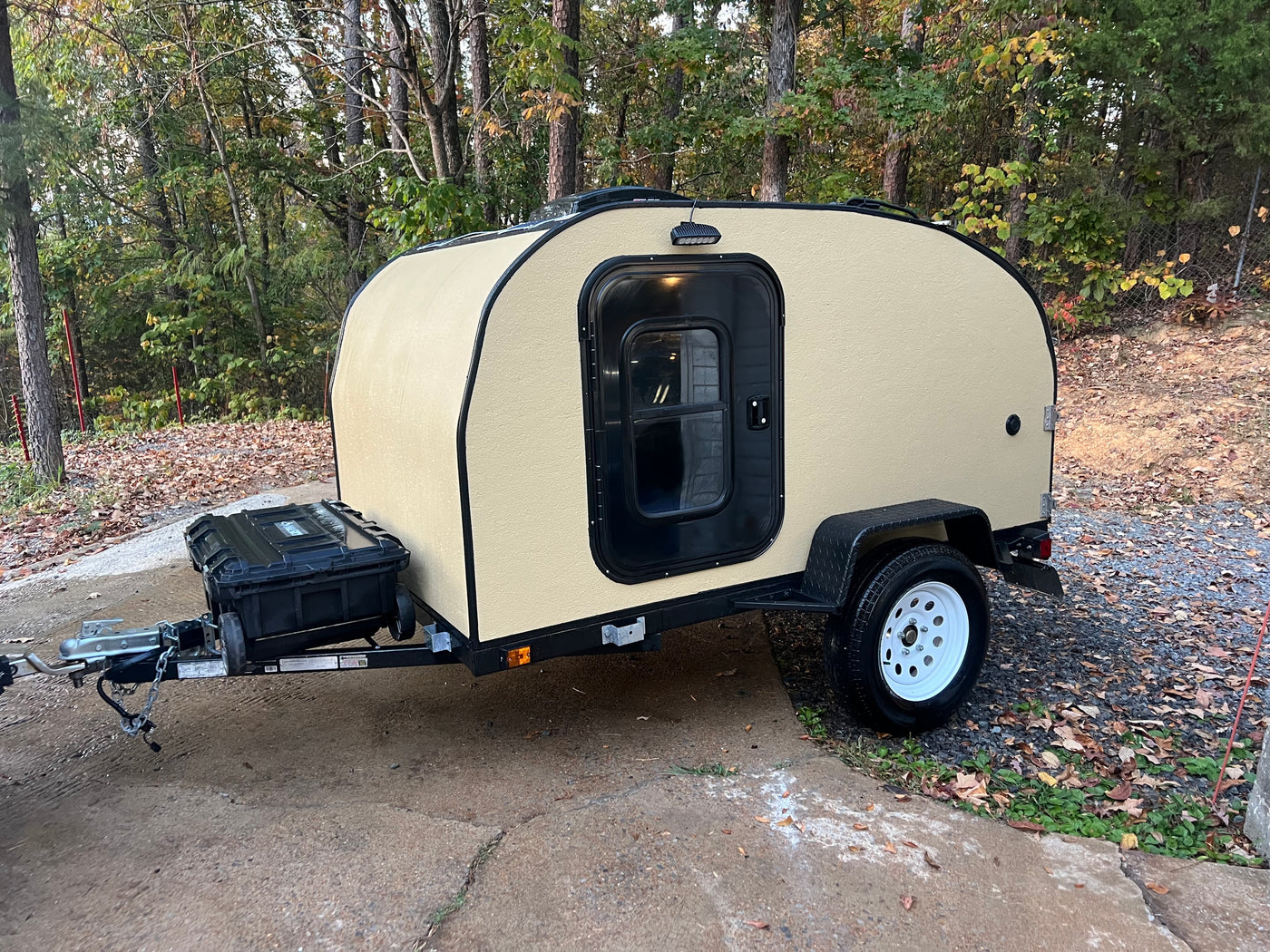 Tan teardrop camper trailer parked on a paved driveway, surrounded by trees. Ideal RV rental for outdoor trips. — photo 2