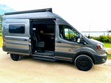 Explore with this grey camper van RV rental parked by a lake. Its side door is open, revealing a custom interior.