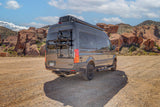 Dark grey Tranquility camper van rv rental in a scenic, rocky desert landscape under a blue sky, perfect for outdoor adventures.