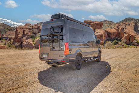 Dark grey Tranquility camper van rv rental in a scenic, rocky desert landscape under a blue sky, perfect for outdoor adventures.