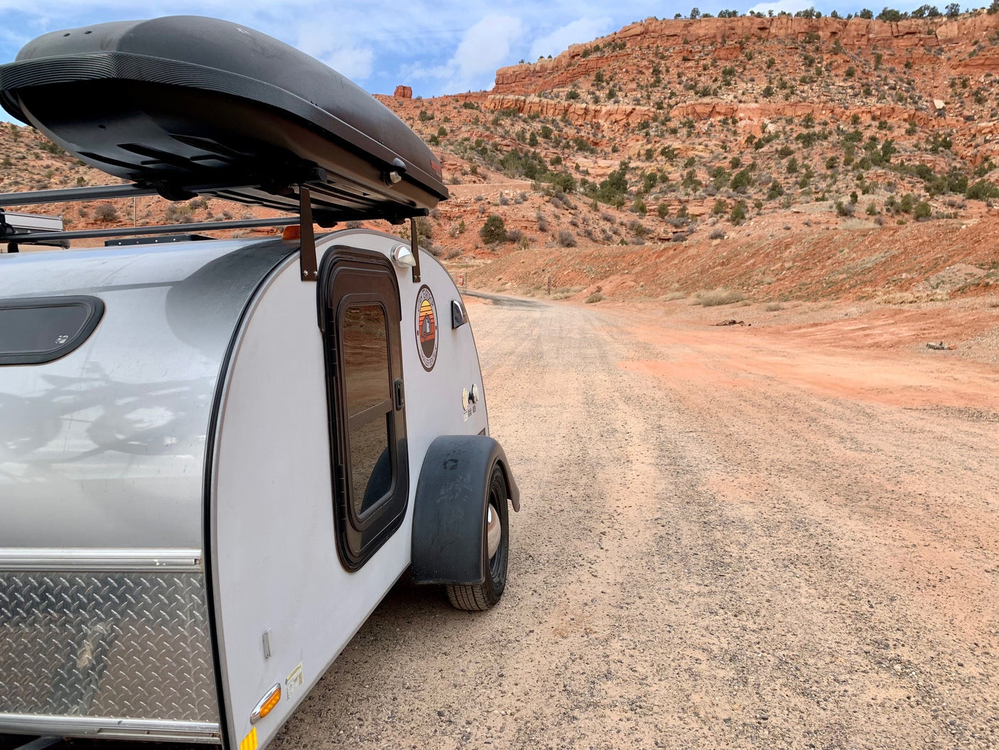 Explore nature with an RV rental! Small teardrop camper on a gravel road, backed by majestic red rock desert mountains.