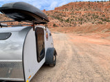 Explore nature with an RV rental! Small teardrop camper on a gravel road, backed by majestic red rock desert mountains.