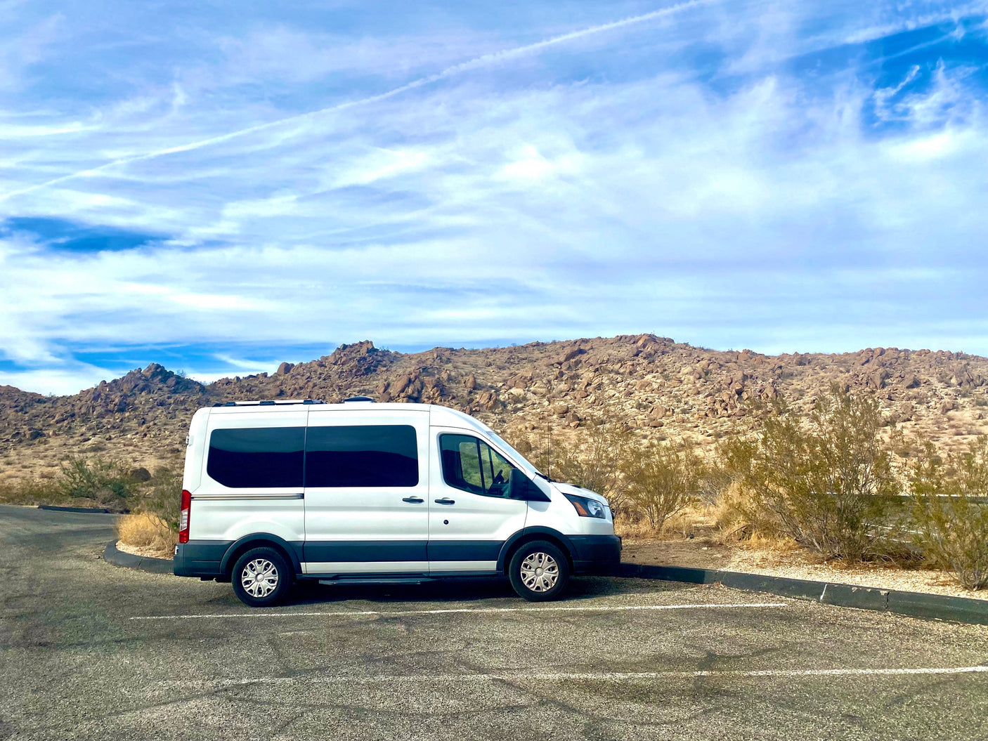 White RV rental van parked in a desert landscape with rocky hills under a blue sky.
