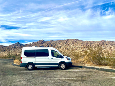White RV rental van parked in a desert landscape with rocky hills under a blue sky.