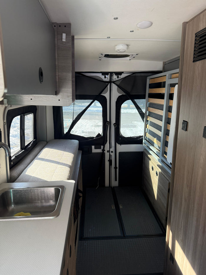 Inside a modern rv rental: kitchen sink, bench bed, overhead cabinets, and rear screens for adventure. Sunlight fills the space.