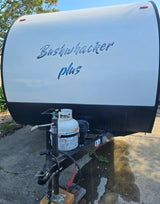 Bushwhacker Plus rv rental: Front of a white travel trailer with a propane tank and hitch assembly, parked on concrete.