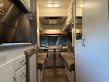 Step inside this cozy rv rental! Features a compact kitchen, comfortable dining area with bench seats, and smart storage solutions.