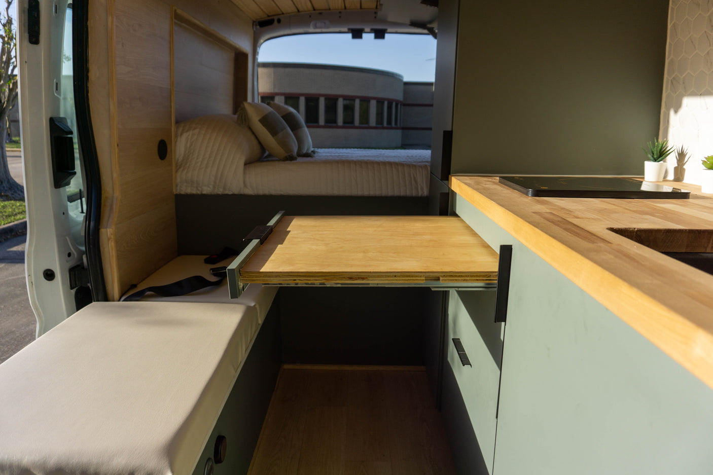 Inside this modern RV rental, see the pull-out dining table, kitchen counter with cooktop, cozy bed, and bench seating.