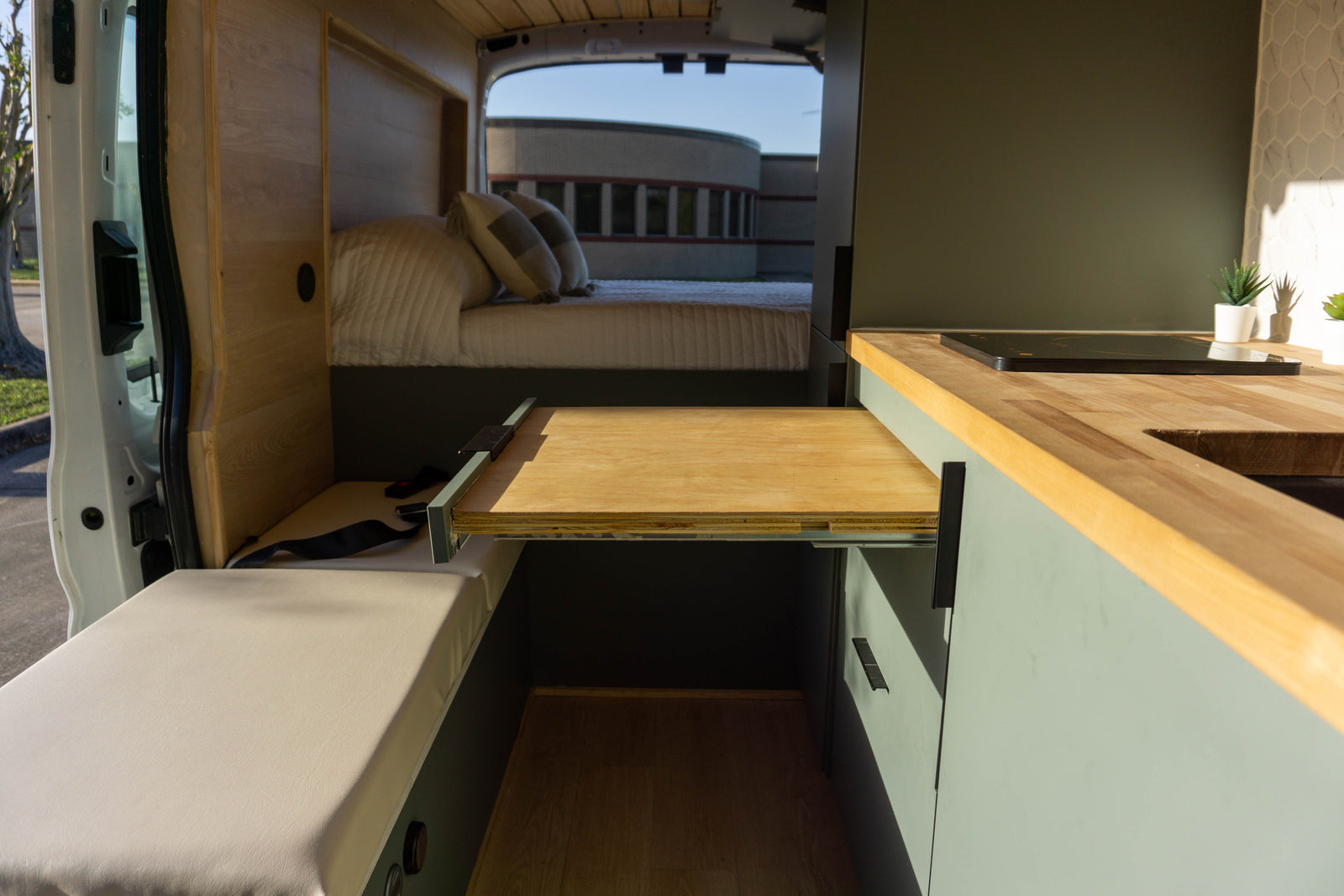 Inside this modern RV rental, see the pull-out dining table, kitchen counter with cooktop, cozy bed, and bench seating.