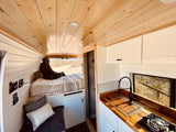 Spacious & cozy rv rental interior with wooden ceilings, kitchen, and bed, perfect for van life adventures.