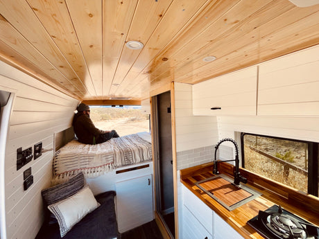 Spacious & cozy rv rental interior with wooden ceilings, kitchen, and bed, perfect for van life adventures.