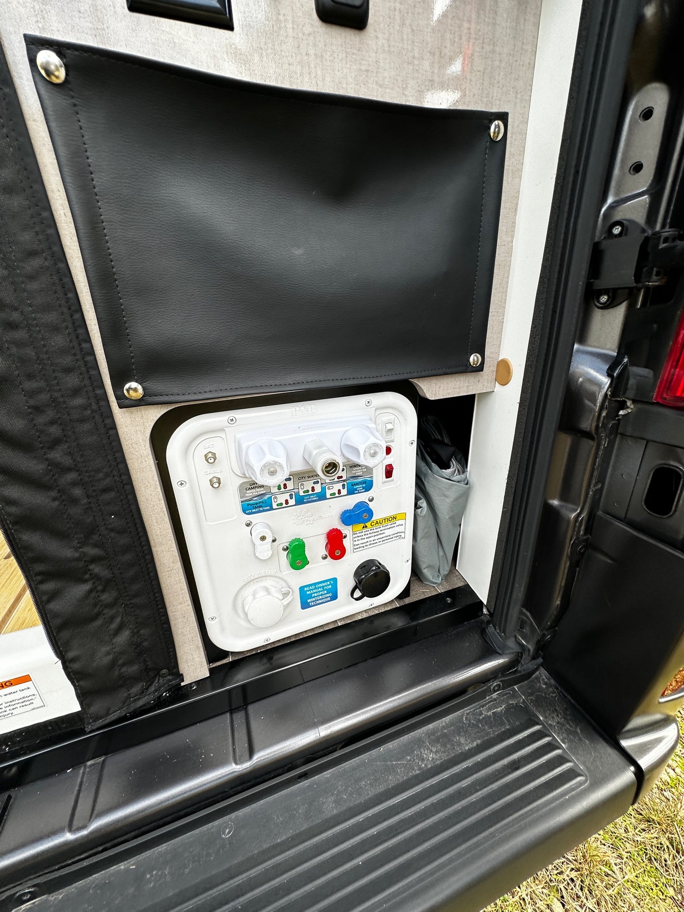 Inside an RV rental's compartment: a white utility panel with color-coded water valves, hose connections, and instructions.