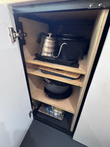 Inside an rv rental, this kitchen cabinet neatly stores a gooseneck kettle, pans, & cutting boards on wood shelves.