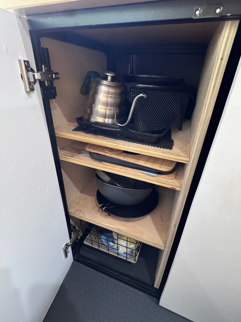 Inside an rv rental, this kitchen cabinet neatly stores a gooseneck kettle, pans, & cutting boards on wood shelves. — photo 7