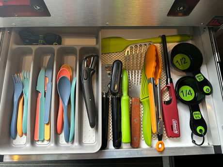 An organized RV rental kitchen drawer showcases a variety of essential cooking utensils, measuring cups, and colorful flatware.