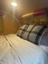 RV rental bedroom: cozy bed with plaid pillows, white duvet, and warm light in the wooden interior.