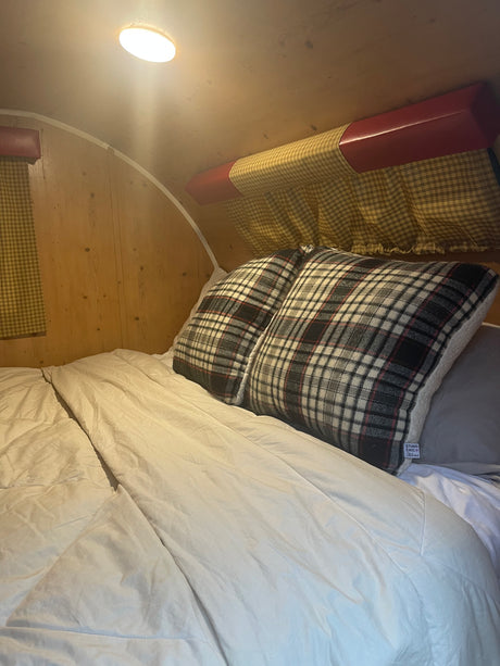 RV rental bedroom: cozy bed with plaid pillows, white duvet, and warm light in the wooden interior.