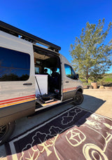 This RV rental, a Storyteller Overland van, is set up for van life with an outdoor kitchen and mat.