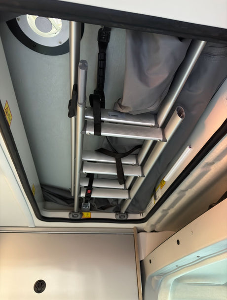 RV rental: Upward view of a stowed collapsible ladder in an RV's pop-top sleeping area, secured for travel.
