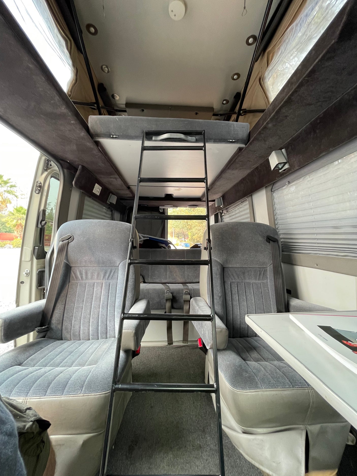 RV rental interior: Functional camper van showing front seats, a ladder to an upper bunk bed, and a rear bench seat.
