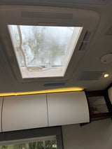 RV rental interior features a rainy skylight with trees, bright overhead cabinets, accent lighting, and air vents.