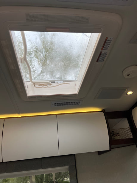 RV rental interior features a rainy skylight with trees, bright overhead cabinets, accent lighting, and air vents.