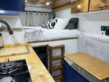 This cozy RV rental interior features a compact kitchen, elevated bed with a ladder, and a convertible dining area.