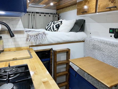 This cozy RV rental interior features a compact kitchen, elevated bed with a ladder, and a convertible dining area.