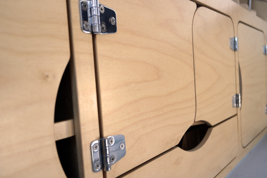 RV rental interior showcasing light wood cabinets, chrome hinges, and unique cut-out handles.