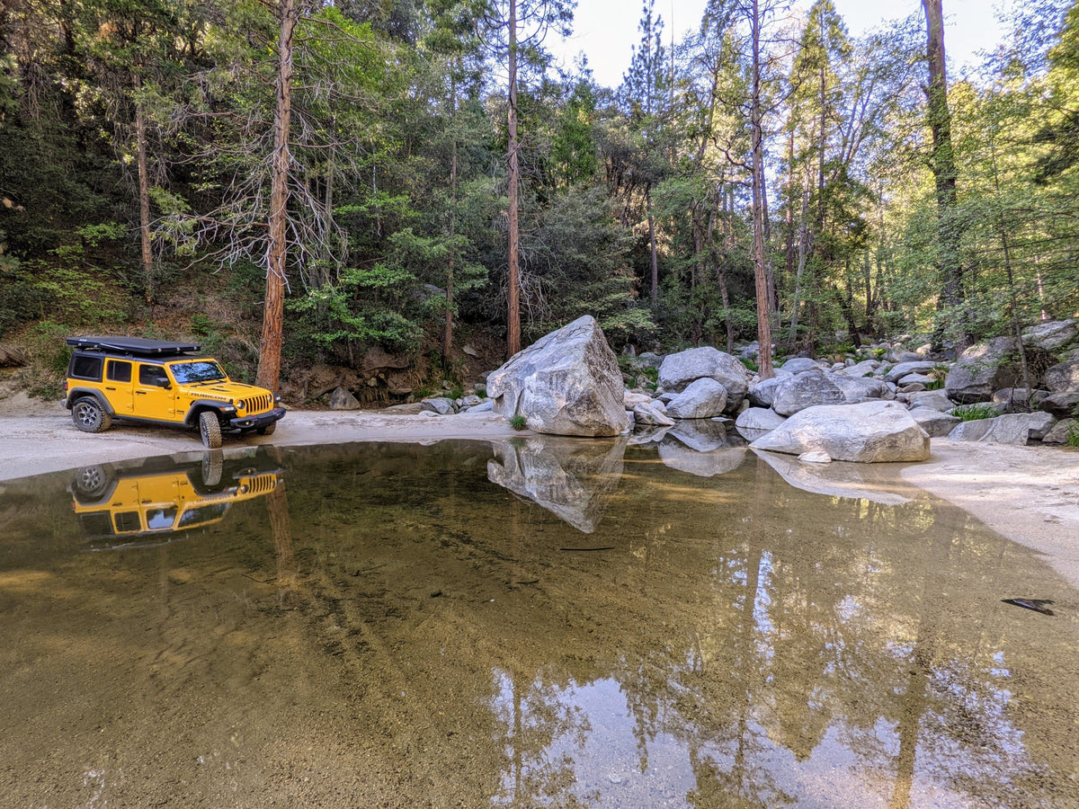  driving through water; an ideal RV rental for off-road adventures.|Yellow Jeep Wrangler with a rooftop tent pitched by a river — photo 14