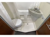 Compact RV rental bathroom with a white toilet, corner sink, and shower pan with curtain.