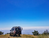 RV rental van with bike parked on a mountain, overlooking a vast sea of clouds under a clear blue sky. Adventure awaits!