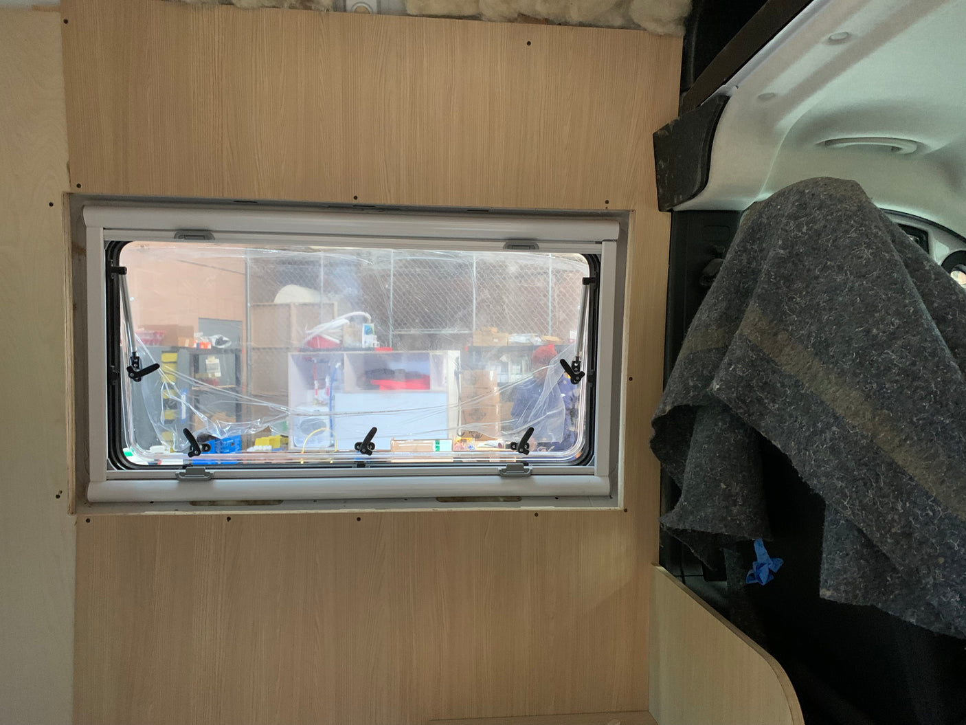 RV rental: Camper interior build with new window, wood paneling, and insulation. Window reveals a workshop view.