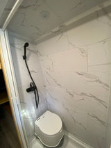 RV rental: Bright, compact bathroom with white marbled walls, black shower head, and white portable toilet.