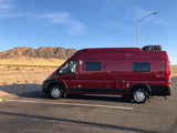 Red RV rental parked in a desert landscape with mountains in the background under a blue sky, ready for adventure.
