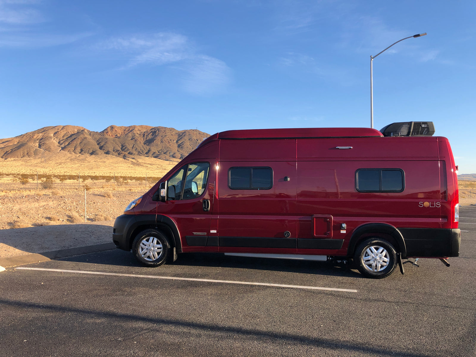 Red RV rental parked in a desert landscape with mountains in the background under a blue sky, ready for adventure.