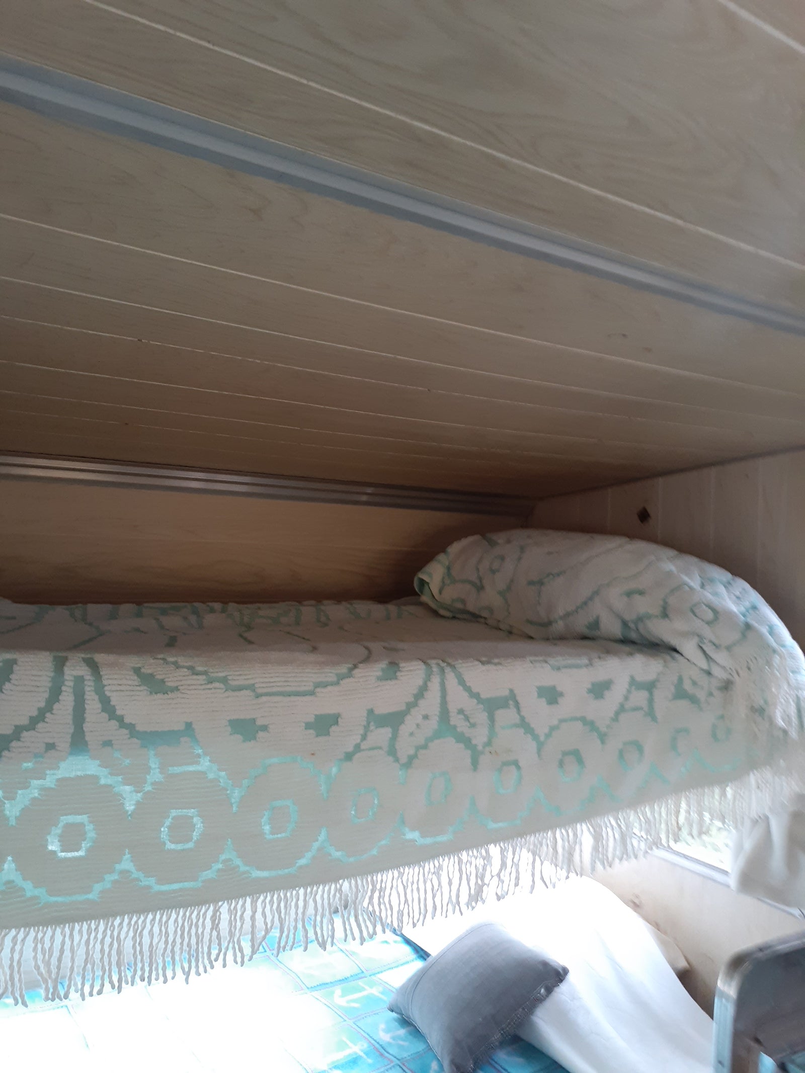 Cozy RV rental interior featuring light wood paneling, a white and teal patterned blanket, and a comfy bed.