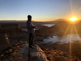A man stands on a cliff overlooking a sunset over a sprawling canyon lake. Imagine this scenic view with your RV rental!