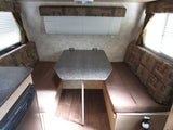 Explore this RV rental's dinette, featuring comfortable benches, a speckled table, and bright windows with blinds.