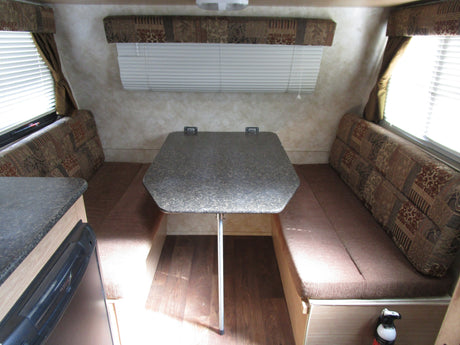 Explore this RV rental's dinette, featuring comfortable benches, a speckled table, and bright windows with blinds.